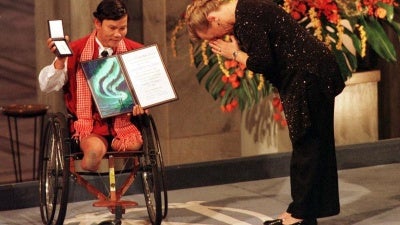 A vencedora do Prêmio Nobel da Paz, Jody Williams, se curva diante do cambojano Tun Channereth, que segura o diploma e a medalha da Campanha Internacional Para Proibir as Minas Terrestres, a caminho de receber o Prêmio Nobel da Paz na Prefeitura de Oslo, em 10 de dezembro de 1997.