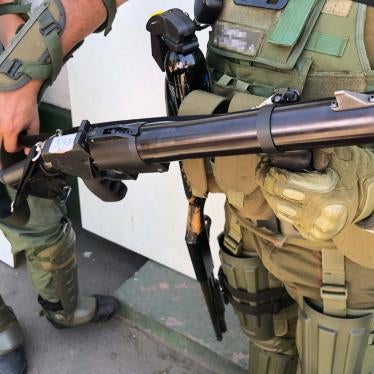 A police captain holds a teargas gun. A pellet shotgun hangs on his right side.